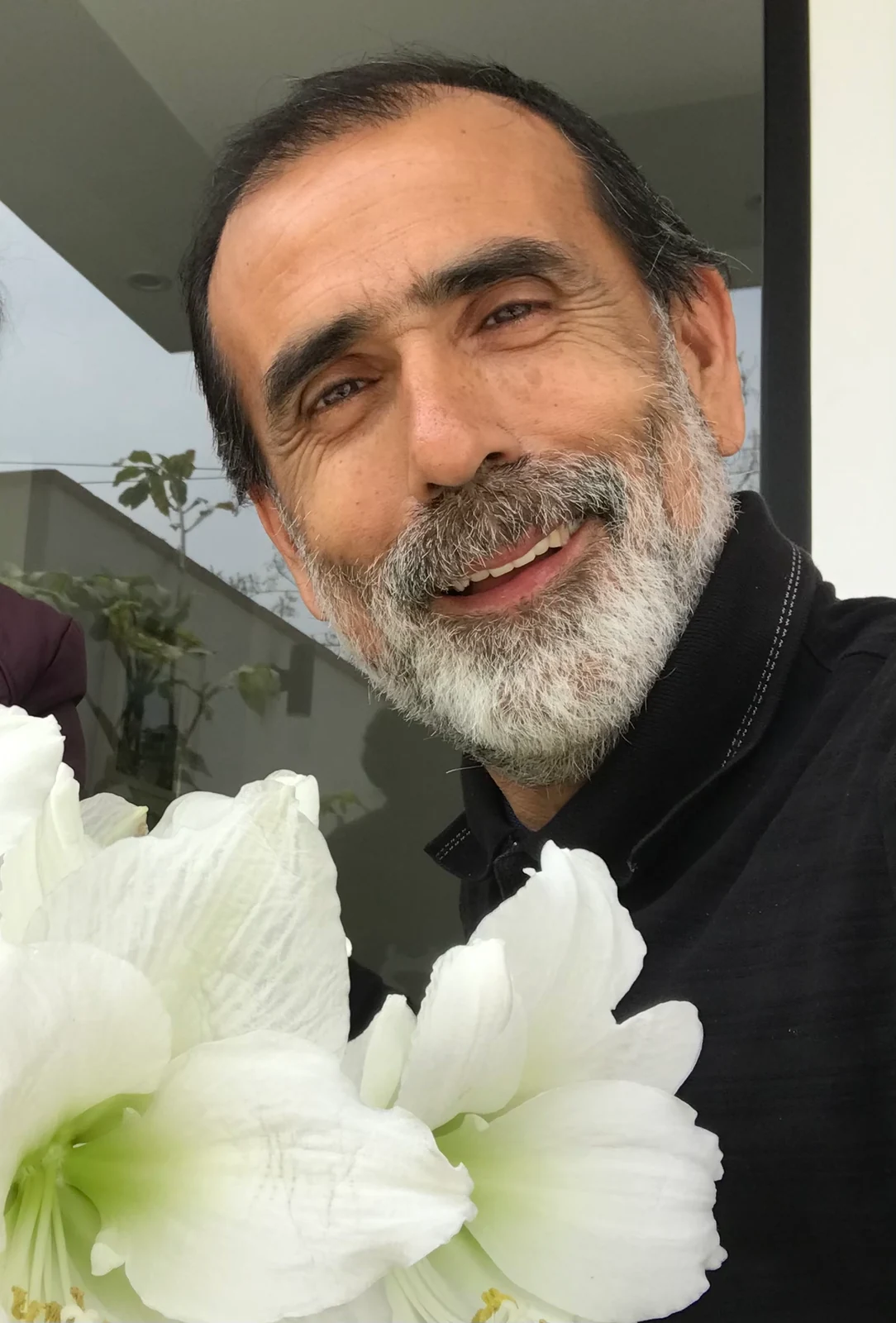 Fernando Novoa smiling beside white flowers, from his personal collection.