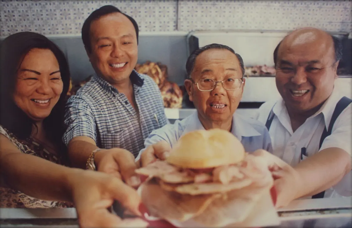 Four smiling adults present a sandwich at El Chinito; official restaurant photograph.