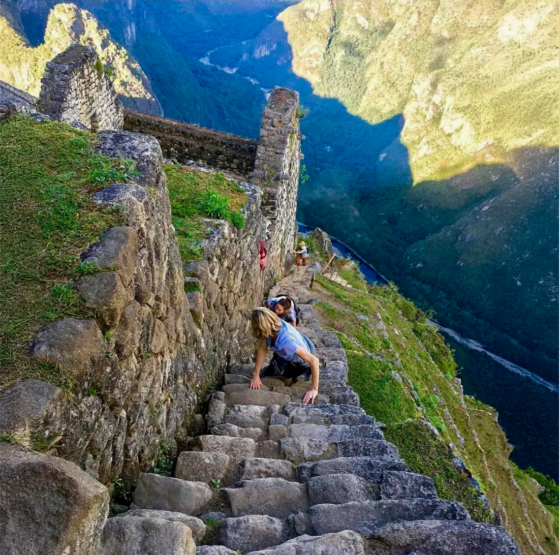 Hikers on a very steep stone stairway beside Inca walls on Huayna Picchu